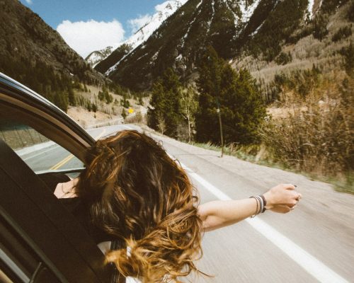 woman riding on vehicle putting her head and right arm outside the window while travelling the road